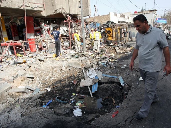 An Iraqi man walks past municipality workers cleaning up debris in the aftermath of a car bombing in the Karrada commercial district in Baghdad, on April 18, 2014. The attack killed at least three people and wounded at least 12 as yesterday was the deadliest day for the Iraqi army since February 11, when 17 soldiers were killed. AFP PHOTO / ALI AL-SAADI