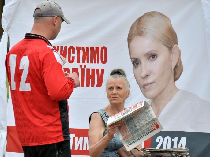 A supporter of Ukrainian presidential candidate Yulia Tymoshenko gives out newspapers and leaflets in front of a campaigning tent with Tymoshenko's portrait on it, in the centre of Kiev on May 23, 2014, two day before Ukraine's presidential election. Ukraine's presidential candidates will hold their final rallies on May 23 as pre-election clouds darkened after the army lost 18 soldiers in attacks by pro-Russian separatists in the country's east. AFP PHOTO / SERGEI SUPINSKY