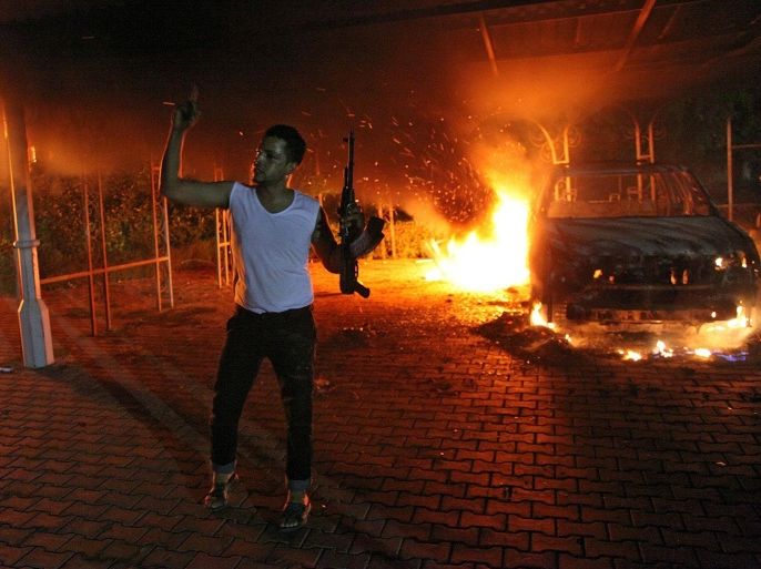 This file photo taken on September 11, 2012 shows an armed man waving his rifle as buildings and cars are engulfed in flames after being set on fire inside the US consulate compound in Benghazi. A long-awaited inquiry into a deadly militant attack on the US mission in the Libyan city of Benghazi late on December 18, 2012 slammed State Department security arrangements there as 'grossly inadequate.' But the months-long probe also found there had been 'no immediate, specific' intelligence of a threat against the mission, which was overrun on September 11 by dozens of heavily armed militants who killed four Americans.