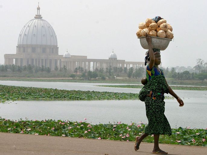 epa00137325 (FILE) An Ivorian woman carrying her baby and a bowl of coconuts walks infront of the giant Basilica in the capital Yamoussoukro, Sunday 15 February 2004. Completed in 1989, the Basilica is the tallest church in the world and cost around US$ 300 million at the time which matched half the national budget deficit which enraged humanitarians as much of the country is still underdeveloped and a high rate of poverty exists. Although Ivory Coast's civil war, sparked by a failed coup in September 2002, was declared officially over in July 2003, the world's top cocoa grower is still split between the rebel-held north and the government-controlled south. EPA/NIC BOTHMA