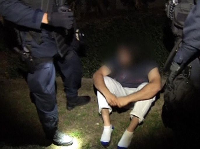 A man detained during a raid sits on the ground between police officers in Sydney, in this still image taken from a police handout video September 18, 2014. Intelligence showed that militants connected with Islamic State were planning to behead a member of the public in Australia, Prime Minister Tony Abbott said on Thursday after hundreds of police raided homes in a sweeping counter-terrorism operation. More than 800 police were involved in the pre-dawn security operation in Sydney and Brisbane, described as the largest in Australian history. At least 15 people had been detained, police told a news conference. Face masked at source. REUTERS/Australian Federal Police Handout via Reuters TV (AUSTRALIA - Tags: POLITICS CIVIL UNREST CRIME LAW) ATTENTION EDITORS - THIS PICTURE WAS PROVIDED BY A THIRD PARTY. REUTERS IS UNABLE TO INDEPENDENTLY VERIFY THE AUTHENTICITY, CONTENT, LOCATION OR DATE OF THIS IMAGE. FOR EDITORIAL USE ONLY. NOT FOR SALE FOR MARKETING OR ADVERTISING CAMPAIGNS. NO SALES. NO ARCHIVES. THIS PICTURE IS DISTRIBUTED EXACTLY AS RECEIVED BY REUTERS, AS A SERVICE TO CLIENTS