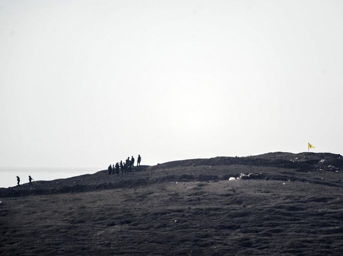 Kurdish fighters stand by a flag of the People's Protection Units (YPG) on Tilsehir hill near the Turkish border after an air strike last night against Islamic State (IS) on October 24, 2014 at the Yumurtalik village, in Sanliurfa province. Turkey said on October 21 that Kurdish peshmerga fighters based in Iraq have yet to cross into Syria from Turkish territory, a day after announcing it was assisting their transit to join the battle for the Syrian town of Kobane, also known as Ain al-Arab. It was seen as a major switch in policy by Turkey, which until now has refused to interfere in the over month-long battle for Kobane between Syrian Kurdish fighters and Islamic State (IS) jihadists. AFP PHOTO / BULENT KILIC