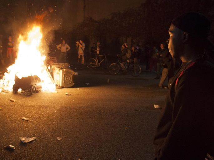 A protester pauses near a bonfire set during a protest against the St. Louis County grand jury decision not to bring criminal charges against Darren Wilson, in Oakland, California, USA, 24 November 2014. The grand jury has decided there was 'no probable cause' to indict Darren Wilson, the white police officer who killed unarmed African-American teenager Michael Brown in an August shooting in Ferguson, Missouri, St Louis County prosecutor Robert McCulloch said.