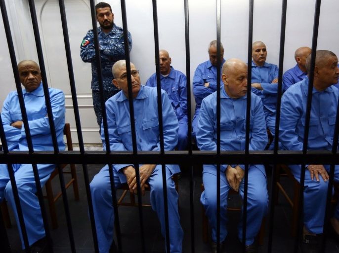 Former Libyan intelligence chief Abdullah al-Senussi (L), dressed in prison blues, sits along with other defendants behind the bars of the accused cell during a hearing as part of his trial in a courthouse in Tripoli on December 28, 2014. Thirty-seven former Kadhafi regime officials are charged with murder, kidnapping, complicity in incitement to rape, plunder, sabotage, embezzlement of public funds and acts harmful to national unity. AFP PHOTO / MAHMUD TURKIA