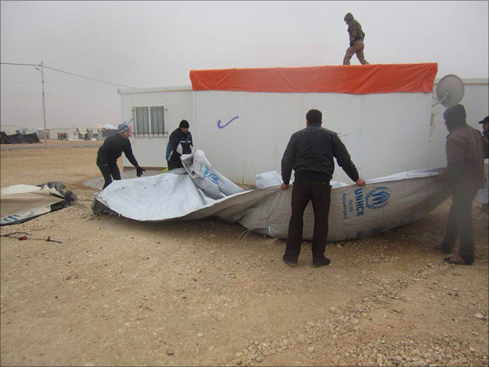 ‪‬ لاجئون يقومون بتثبيت إحدى الخيام التي اقتلعتها الرياح(الجزيرة)