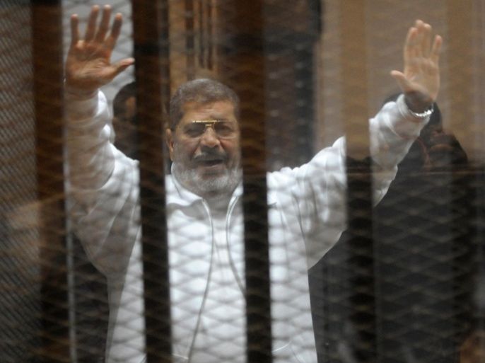 Egypt's deposed Islamist president Mohamed Morsi waves from inside the defendants cage during his trial at the police academy in Cairo on January 8, 2015. An Egyptian court is to deliver a verdict on April 21 in the trial of Morsi and 14 others charged with inciting the killing of protesters, judicial officials said. AFP PHOTO / STR