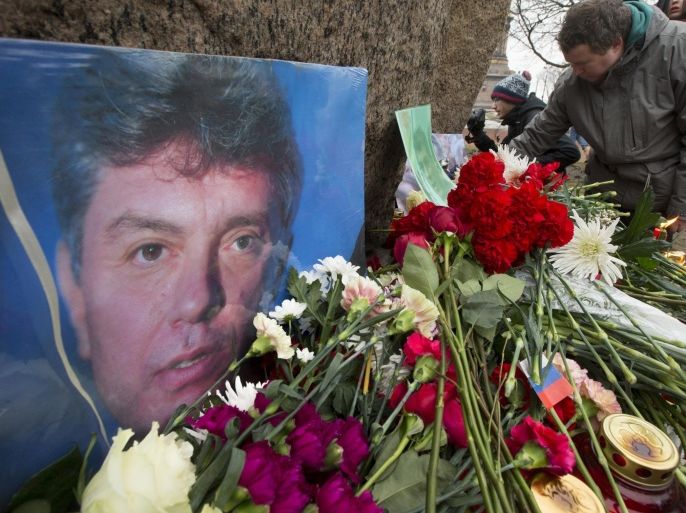 People lay flowers in memory of Boris Nemtsov, seen at left, at the monument of political prisoners 'Solovetsky Stone' in central St. Petersburg, Russia, Saturday, Feb. 28, 2015. Nemtsov was gunned down Saturday near the Kremlin, just a day before a planned protest against the government. (AP Photo/Dmitry Lovetsky)