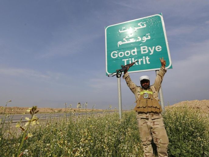 A Shi'ite fighter gestures in front of a billboard on a street in the town of al-Alam March 9, 2015. Just north of Tikrit, home city of executed Sunni former president Saddam Hussein, Iraqi security forces and Shi�ite militia fighters began an offensive against Islamic State to regain control over the town of al-Alam. REUTERS/Thaier Al-Sudani (IRAQ - Tags: POLITICS CIVIL UNREST CONFLICT)