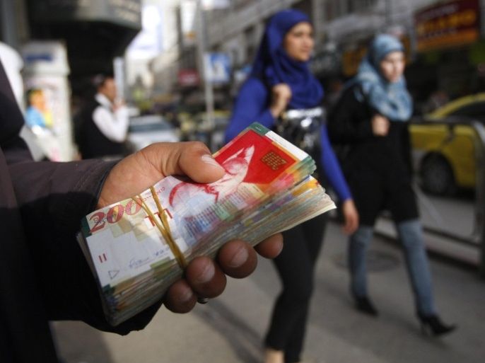 Palestinian women walk past a money changer in the West Bank city of Ramallah February 16, 2010. The Palestinians do not have their own currency. The dollar and the Jordanian dinar are both used for some transactions, though the Israeli shekel is most commonly handled in day-to-day cash transactions.