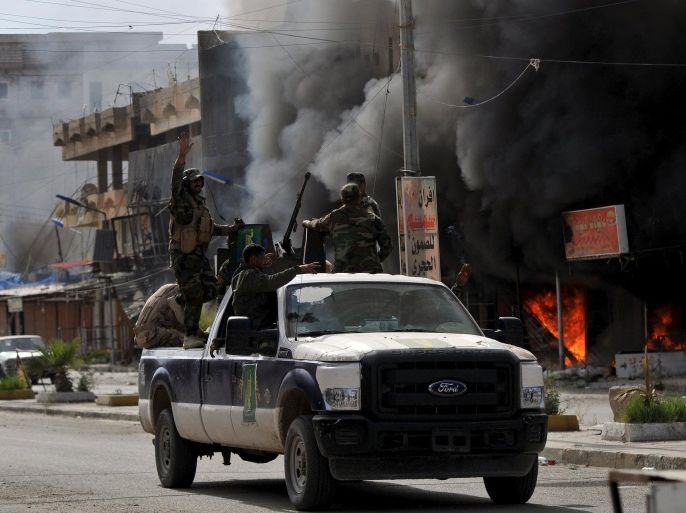 Members of Hashid Shaabi forces ride in a vehicle as smoke rises in shops at al-Qadisiya neighborhood, north of Tikrit April 3, 2015. REUTERS/Stringer