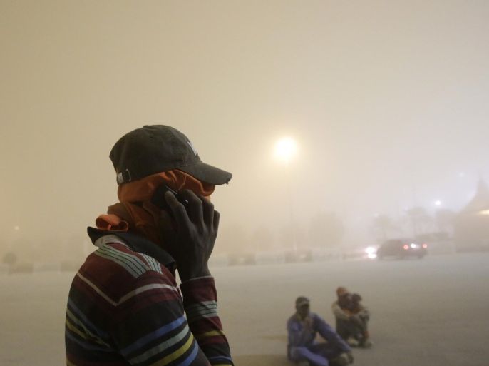 Asian laborers cover their faces from the dust as they wait for their ride just outside the Bahrain International Circuit in Sakhir, Bahrain, Wednesday, April 1, 2015. A sudden and strong sand storm hit the tiny Gulf island nation Wednesday evening. Incoming flights were suspended, the official Bahrain News Agency reported, but departures continued as of late Wednesday. (AP Photo/Hasan Jamali)