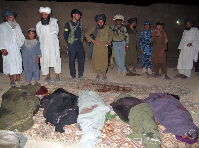 People stand beside the bodies of the victims who were killed when their passenger van hit a landmine in Marjah district in restive Helmand province, Afghanistan, 21 June 2015. At least 21 civilians, most of them from the same family, were killed in the incident.