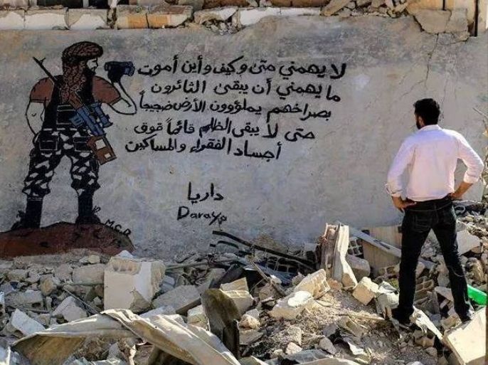 أبو مالك يتأمل إحدى لوحاته على الجدران في مدينة داريا المحاصرة بريف دمشق