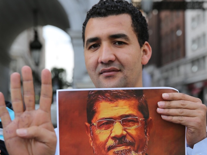 ‪متظاهر في لندن يحمل صورة مرسي ويرفع شعار رابعة‬ (غيتي)