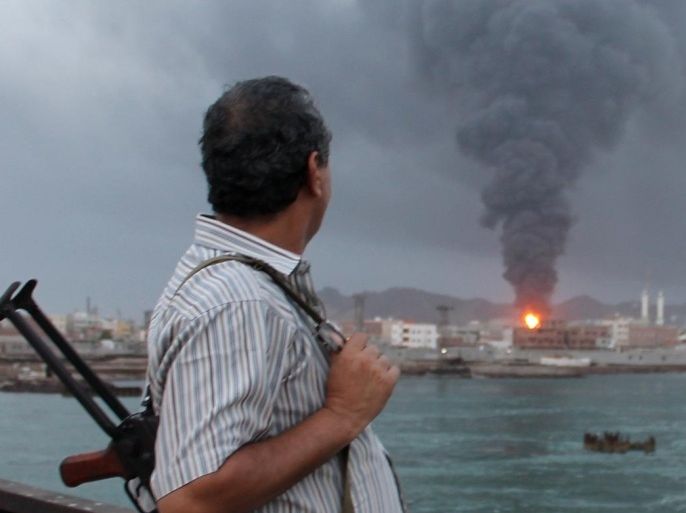 An armed Yemeni man looks at fire and smoke rising from the Aden oil refinery following a reported shelling attack by Shiite Huthi rebels in the embattled southern Yemeni city of Aden on July 13, 2015. Clashes have intensified in Aden, where rebels have besieged many areas controlled by southern fighters loyal to exiled President Abedrabbo Mansour Hadi and known as the Popular Resistance. AFP PHOTO / SALEH AL-OBEIDI