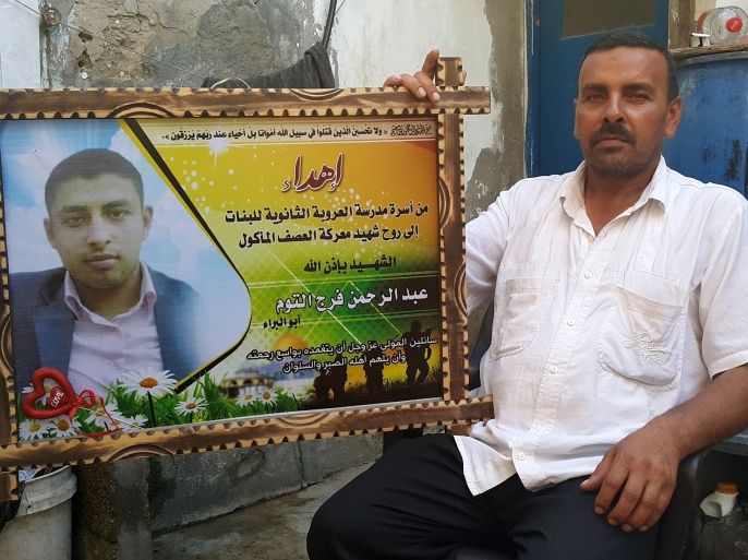 فرج الله التوم يجلس إلى جانب صورة ابنه الشهيد عبد الرحمن في مخيم النصيرات بقطاع غزة