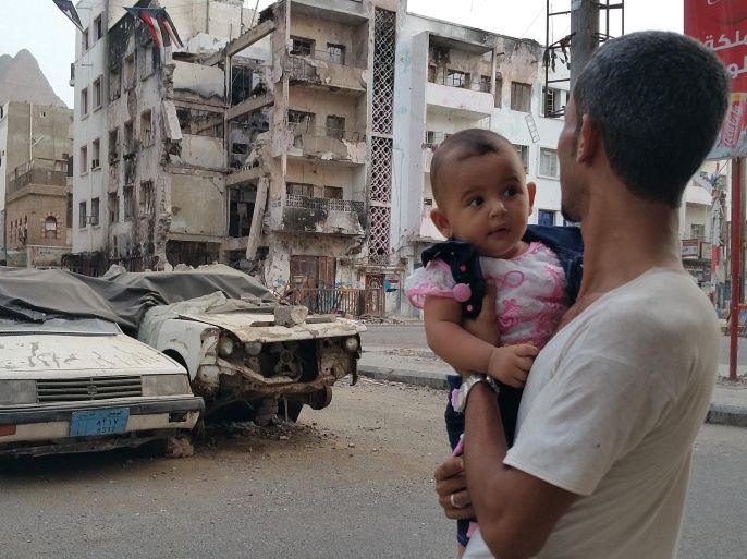 A Yemeni man carrying his daughter looks at a building destroyed during fighting against Houthi fighters in the port city of Aden, Yemen, Sunday, July 19, 2015. Shiite rebels and their allies in Yemen randomly shelled a town Sunday outside of Aden after losing control of some the port city's neighborhoods, killing at least 45 people and wounding 120, officials said. (AP Photo/Ahmed Sameer)