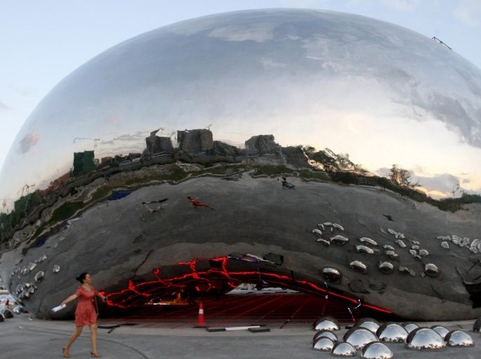 In this photo taken Aug. 9, 2015, residents walk past a giant sculpture in the shape of an oil bubble under construction in the city of Karamay in the China's Xinjiang Uighur Autonomous Region. Renowned British-Indian artist Anish Kapoor has expressed outrage about the appearance of the sculpture in China that appears identical to his "Cloud Gate" in Chicago. (Color China Photo via AP) CHINA OUT