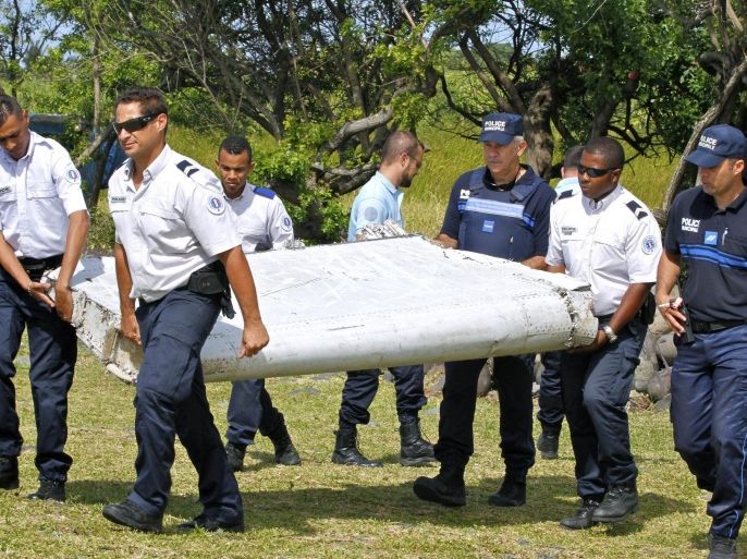 FILE - In this photo dated Wednesday, July 29, 2015, French police officers carry a piece of debris from a plane in Saint-Andre, Reunion Island. Malaysian officials said Sunday, Aug. 2, 2015 that they would seek help from territories near the island where a suspected piece of the missing Malaysia Airlines jet was discovered to try to find more possible debris from the plane. (AP Photo/Lucas Marie, File)