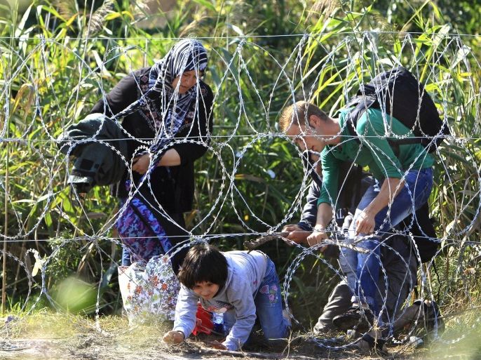 Syrian migrant family cross under a fence as they enter Hungary at the border with Serbia, near Roszke, August 28, 2015. REUTERS/Bernadett Szabo