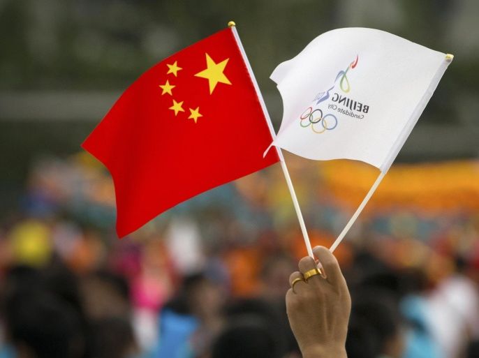 A participant holds Chinese and Beijing 2022 flags before the announcement that Beijing will host the 2022 Winter Olympics at a gathering outside the Beijing Olympic Stadium, also known as the Birds Nest, in Beijing, Friday, July 31, 2015. Beijing was selected Friday to host the 2022 Winter Olympics, becoming the first city awarded both the winter and summer games. (AP Photo/Mark Schiefelbein)