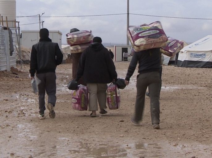لاجئون سوريون يحملون أغطية وزعتها عليهم إحدى المنظمات الدولية مع دخول فصل الشتاء القارس في صحراء الأردن- الجزيرة