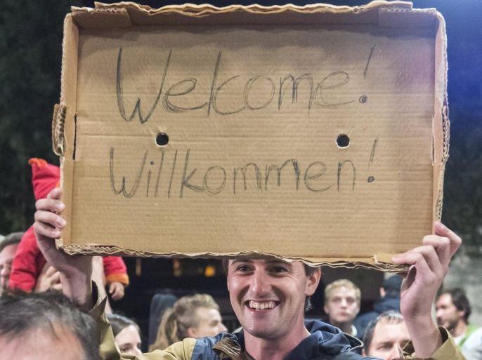 FILE - In this Saturday, Sept. 5, 2015 file photo, a man holds a "Welcome" sign during the arrival of refugees at the train station in Saalfeld, central Germany. Hundreds of refugees arrived in a train from Munich to be transported by busses to an accomodation center. The United States and the European Union project themselves as models for the world when it comes to democracy and human rights. Yet a common issue, migration, is bitterly dividing each of them(AP Photo/Jens Meyer, File)