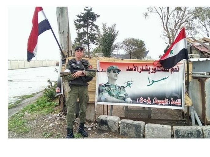 جندي روسي يقف أماملوحة تحمل صورة بشار الأسد بطرطوس