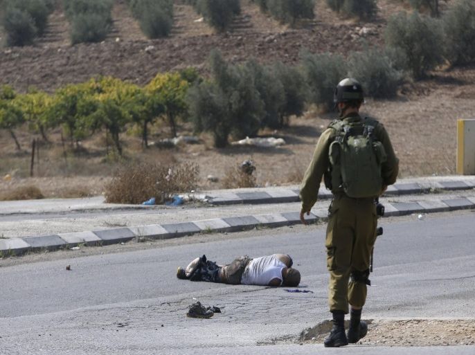 ATTENTION EDITORS - VISUAL COVERAGE OF SCENES OF INJURY OR DEATH An Israeli soldier stands next to an Israeli motorist after he was struck by a Palestinian vehicle in the West Bank city of Hebron October 20, 2015. A Palestinian vehicle ran over and killed an Israeli motorist whom a Reuters photographer said was using a club to hit Palestinian protesters and cars on a roadside in the Israeli-occupied West Bank. Israeli police said the man had stopped his car after stones were thrown at it. The driver of the Palestinian vehicle, which the photographer said the Israeli had hit with his club, later turned himself in to Palestinian police. Neither they nor Israeli police commented immediately on whether they believed he had struck the Israeli deliberately. REUTERS/Mussa Qawasma TEMPLATE OUT.