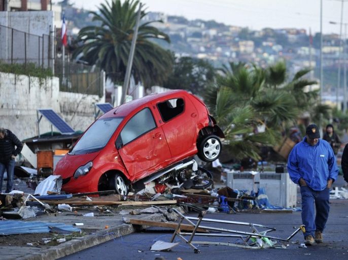 Chileans pass a wrecked car pushed by strong waves, after a magnitude 8.4 Richter scale earthquake, in Coquimbo, Chile, 17 September 2015. According to the Chilean Interior Minister, Jorge Burgos, 17 September the death toll from the 8.4-magnitude quake that hit parts of Chile 16 September has risen to eight, while one person remains missing. The Government has put the entire Chilean coast on high alert over tsunami fears leading to the evacuation of a million people. The sea advanced inland at several points on the Chilean coast, mainly in the region of Coquimbo, where authorities were waiting for daylight to assess the damage caused, as more than 500 people spent the night in shelters. EPA/ALEJANDRO PIZARRO CHILE OUT