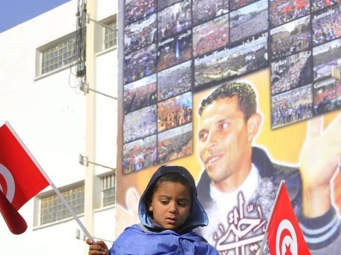 A man carries his child waving Tunisian national flag and passing a billboard bearing the photo of late Tunisian fruit vendor Mohamed Bouazizi, during a demonstration against the visit of Tunisian President Moncef Marzouki on the second anniversary of the Tunisian revolution, in Sidi Bouzid, south Tunisia, 17 December 2012. Young fruit vendor, Mohamed Bouazizi, set himself ablaze on 17 December 2010 in the Tunisian town of Sidi Bouzid, sparking a nation-wide uprising that led 28 days later to the ousting of President Zine Al Abidine Ben Ali, and later to regional revolutions of the so-called Arab Spring. However, two years after the start of the revolution in Tunisia, many people are still frustrated by the slow pace of job creation.