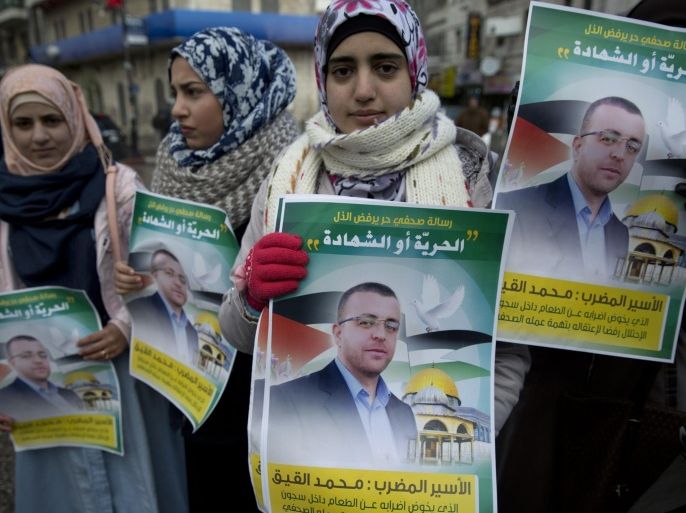 Protesters carry posters with pictures of Palestinian journalist Mohammed al-Qeq, 33, his name and Arabic that reads "the message of a free journalist who rejects humiliation is freedom or martyrdom," during a protest in the West Bank city of Ramallah, Tuesday, Jan. 26, 2016. The health of a Palestinian journalist detained by Israel who has been on a 63-day hunger strike is deteriorating, lawyers and supporters said Tuesday, while the Israeli hospital where he is being held said his condition has not changed significantly in recent days. (AP Photo/Nasser Nasser)