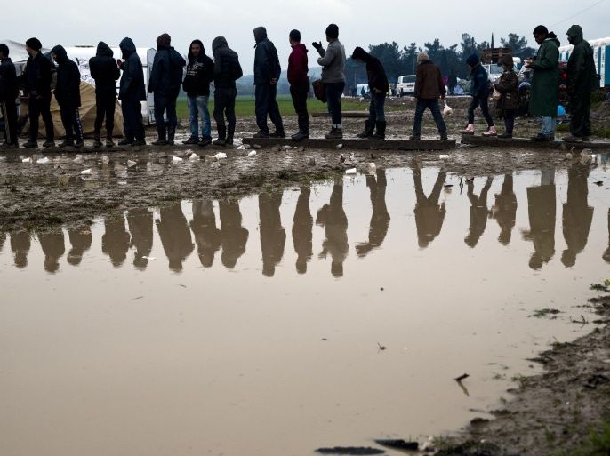 Migrants are reflected in a puddle while waiting in line to receive hot tea, during a rainfall at the northern Greek border point of Idomeni, Greece, Tuesday, March 15, 2016. Hundreds of migrants and refugees walked out Monday of an overcrowded camp on the Greek-Macedonian border Monday, determined to use a dangerous crossing to head north but were returned to Greece.(AP Photo/Vadim Ghirda)