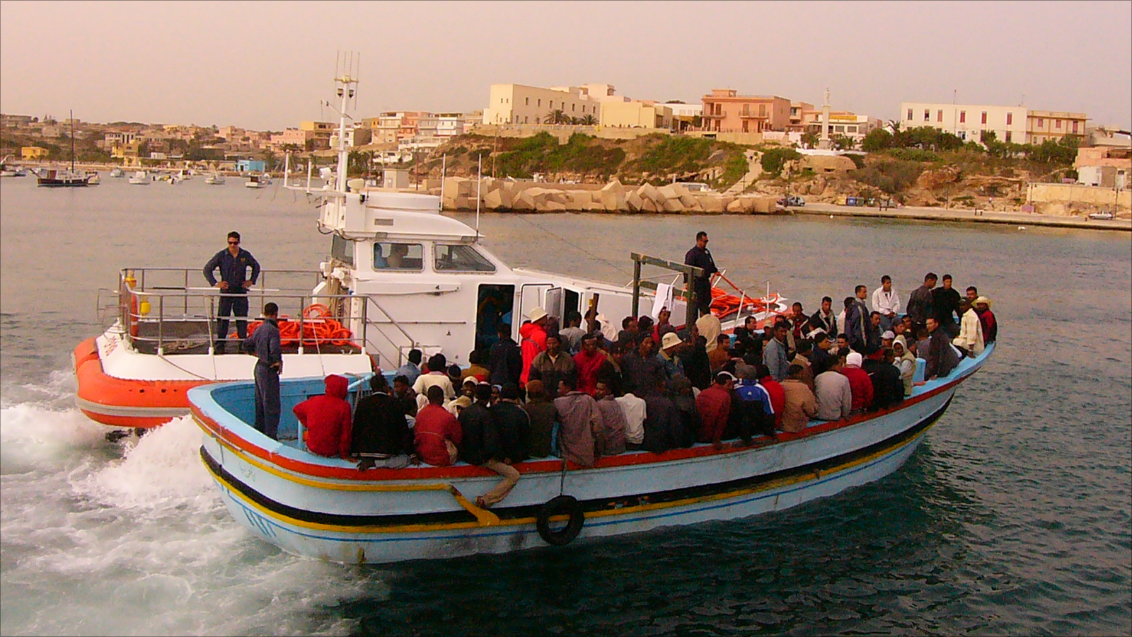 قارب يحمل لاجئين إريتريين وصوماليين قادمين من ليبيا عند دخوله جزيرة لامبيدوزا برفقة خفر السواحل الإيطالي 