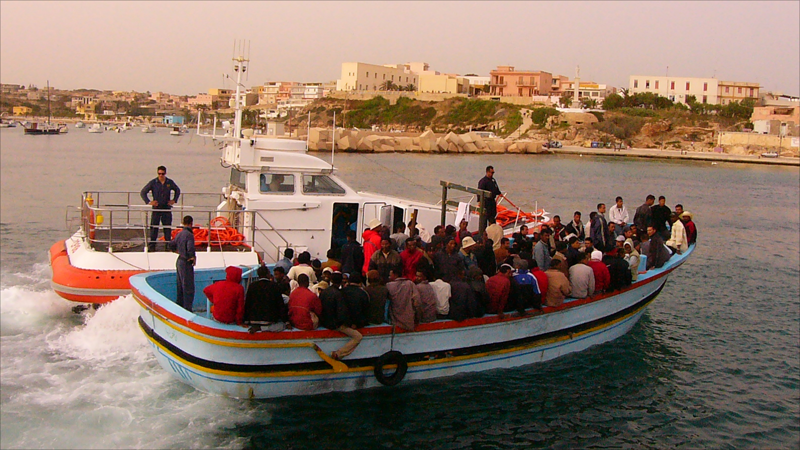 قارب به لاجئون أفارقة عند دخوله جزيرة لامبيدوزا برفقة خفر السواحل الإيطالي (الجزيرة)