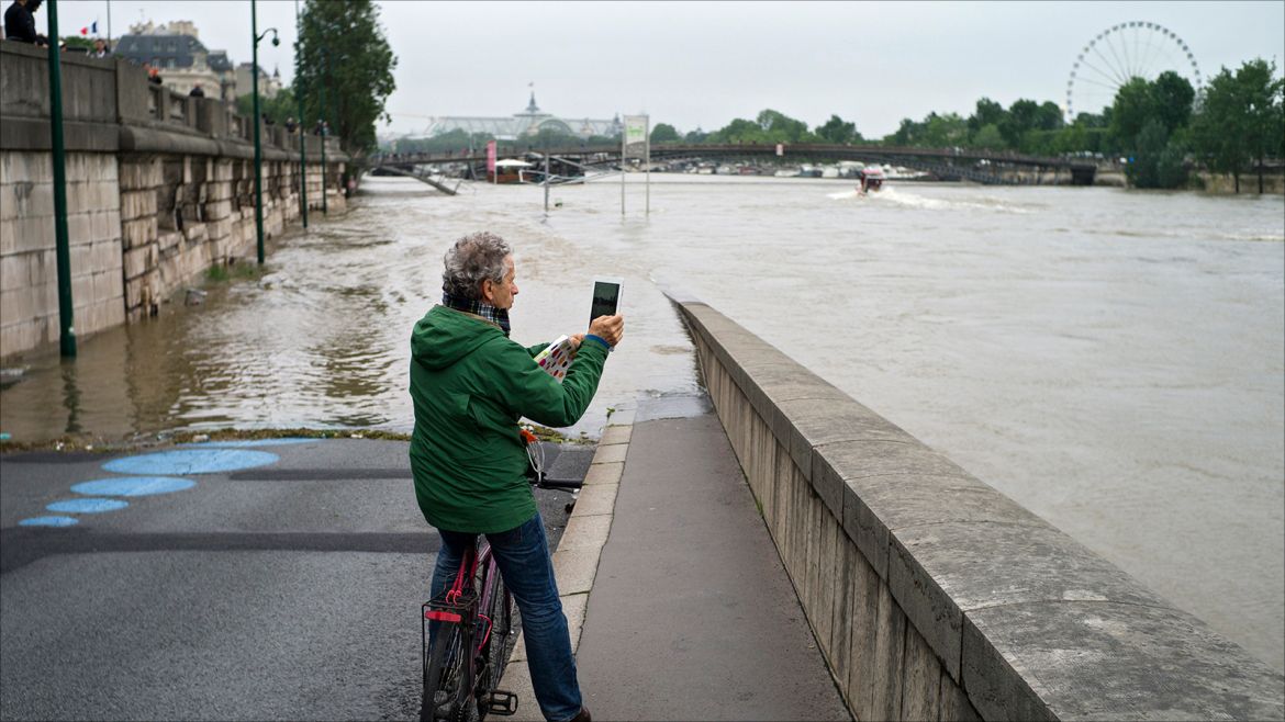 epa05342820 A cyclist takes a pictures of the Seine river submerging a dock in Paris, France, 02 June 2016. Floods and heavy rain drenched about a quarter of the French territory over several days.  EPA/YOAN VALAT