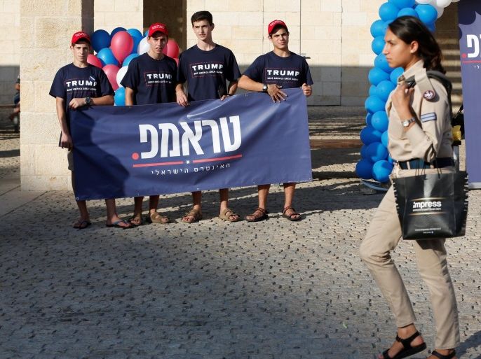 An Israeli soldier walks past members of the U.S. Republican party's election campaign team in Israel, who are holding a banner in support of Republican U.S. presidential nominee Donald Trump, during a campaign aimed at potential American voters living in Israel, near a mall in Modi'in, Israel August 15, 2016. REUTERS/Baz Ratner
