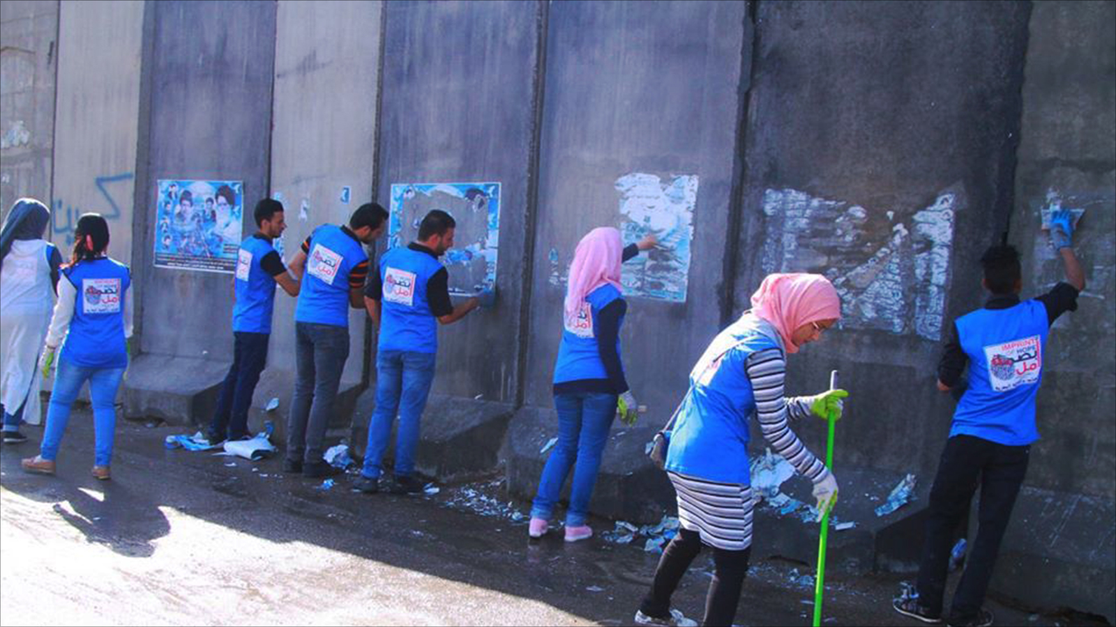 ‪متطوعون من الفريق يقومون بإزالة بعض الملصقات من الكتل الكونكريتية تمهيدا للرسم عليها‬ (الجزيرة)