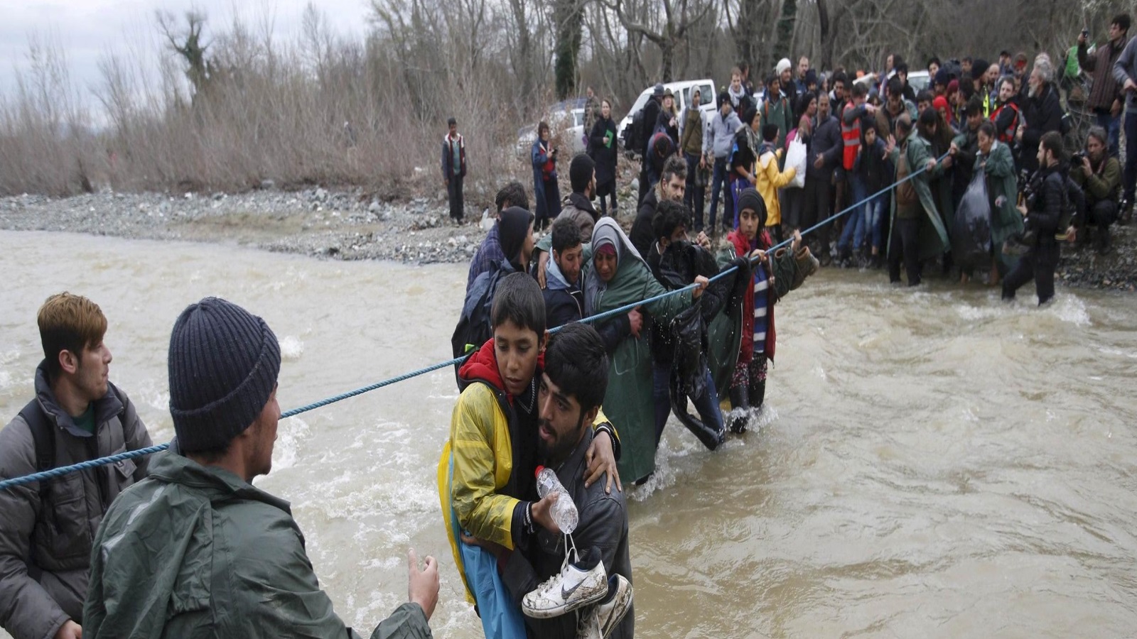 لاجئون يعبرون النهر قرب الحدود اليونانية المقدونية غربي قرية إديوميني اليونانية أوائل 2014 (رويترز)