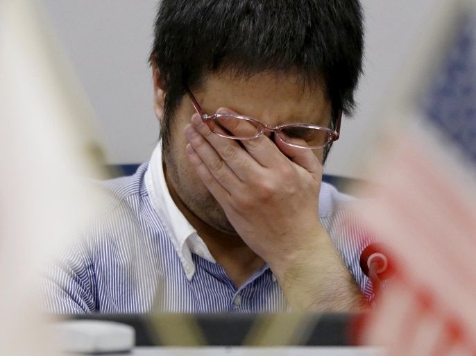 An employee of a foreign currency company wipes his face as he is seen between U.S. (R) and Japanese national flags at a dealing room in Tokyo, Japan, April 7, 2016. REUTERS/Issei Kato