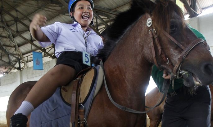 An autistic child reacts while sitting on a horse during the Horse Therapy Special Children program at the Mounted Police Sub-Division in Bangkok June 17, 2014. The program aims to help children with autism and other physical problems develop brain and body coordination and to adapt to their family and community. REUTERS/Chaiwat Subprasom (THAILAND - Tags: SOCIETY ANIMALS HEALTH CRIME LAW)