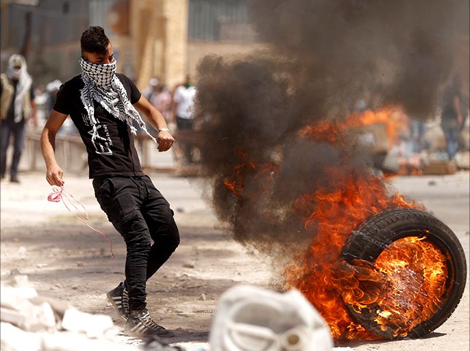 A Palestinian protester moves a burning tyre during clashes with Israeli troops at a protest in support of Palestinian prisoners on hunger strike in Israeli jails, in the West Bank village of Beita, near Nablus April 28, 2017. REUTERS/Mohamad Torokman