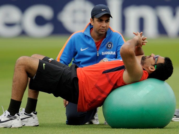 India's Zaheer Khan stretches on a ball watched by the Indian team physiotherapist during a training session before Friday's second cricket test match against England at Trent Bridge in Nottingham July 28, 2011. REUTERS/Philip Brown (BRITAIN - Tags: SPORT CRICKET)