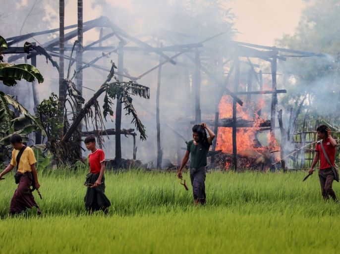 TOPSHOT - In this photograph taken on September 7, 2017, unidentified men carry knives and slingshots as they walk past a burning house in Gawdu Tharya village near Maungdaw in Rakhine state in northern Myanmar. The men were seen by journalists walking past the burning structure during a Myanmar government sponsored trip for media to the region. In the last two weeks alone 164,000 mostly Rohingya civilians have fled to Bangladesh, overwhelming refugee camps that were already bursting at the seams and scores more have died trying to flee the fighting in Myanmar's Rakhine state, where witnesses say entire villages have been burned since Rohingya militants launched a series of coordinated attacks on August 25, prompting a military-led crackdown. / AFP PHOTO / STR (Photo credit should read STR/AFP/Getty Images)