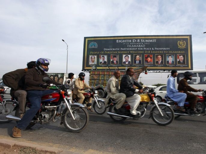 People ride motorcycles past a banner promoting the Eighth D-8 Summit in Islamabad November 21, 2012.Pakistan will hold the Developing-8 summit (D8) on November 22. The D-8 is a group of developing countries with large Muslim populations that have formed an economic development alliance. It consists of Turkey, Pakistan, Egypt, Iran, Bangladesh, Nigeria, Indonesia and Malaysia. REUTERS/Faisal Mahmood(PAKISTAN - Tags: POLITICS) )