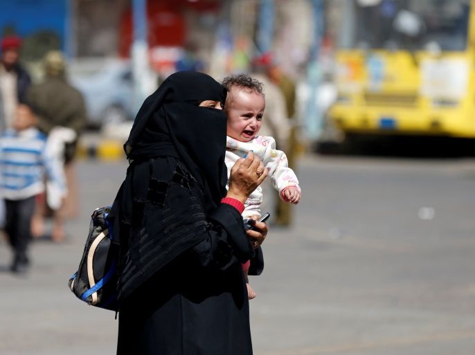 A woman carries a child as she walks by a gathering of Houthi followers celebrating Houthi advancement on forces loyal to Yemen's former president Ali Abdullah Saleh at Tahrir Square in Sanaa, Yemen December 3, 2017. REUTERS/Khaled Abdullah