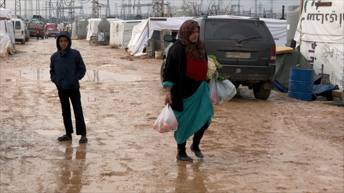 A Syrian refugee woman carries bags with supplies on a muddy road between makeshift shelters and tents in the informal Syrian refugee settlement Amriyeh in Saadnayel, Bekaa Valley, eastern Lebanon, which the European Union's ambassador to Lebanon Christina Lassen visited on 22 December 201