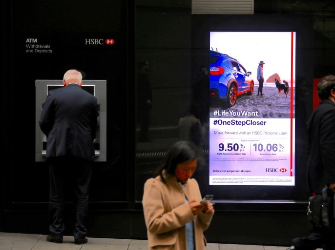 A customer of Europe's biggest bank HSBC uses an ATM next to an illuminated advertisement displaying personal loan rates as two pedestrians walk past smoking cigarettes in central Sydney, Australia, June 20, 2017. REUTERS/David Gray