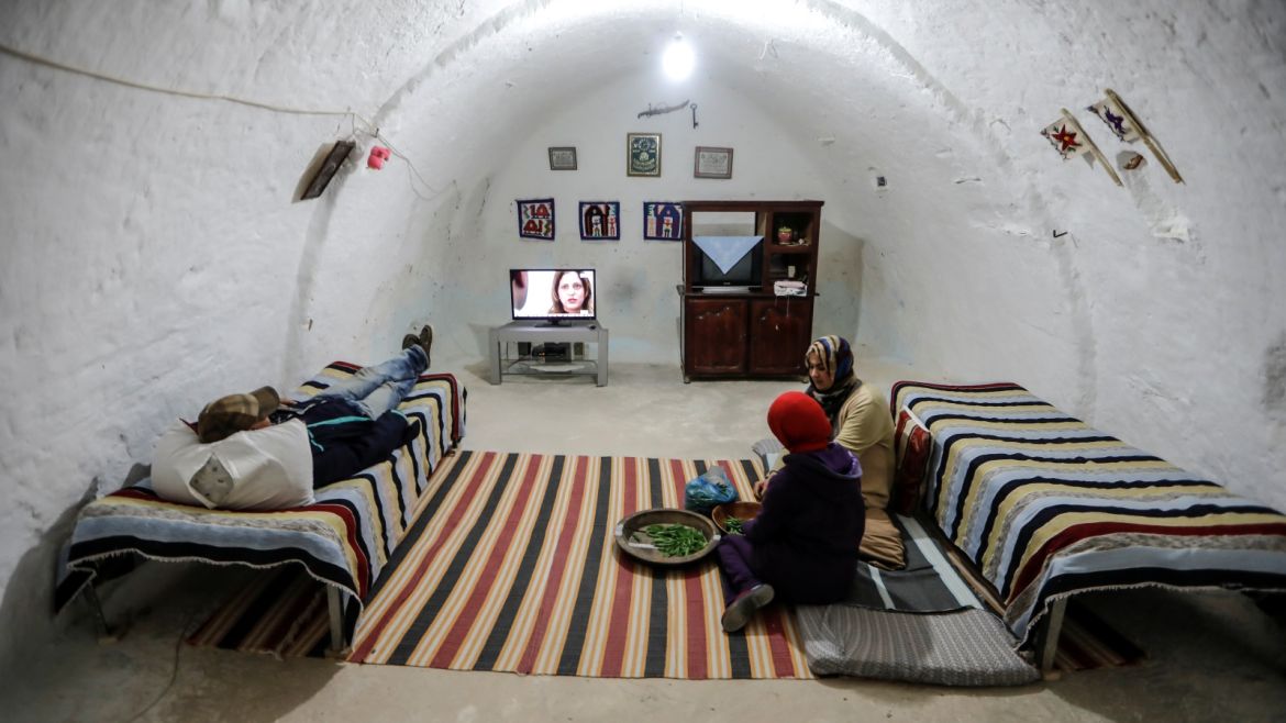 Samar, 18, and Latifa Ben Yahia, 38, (C) shell peas as their brother watches television at their troglodyte house on the outskirts of Matmata, Tunisia, February 3, 2018. REUTERS/Zohra Bensemra  SEARCH