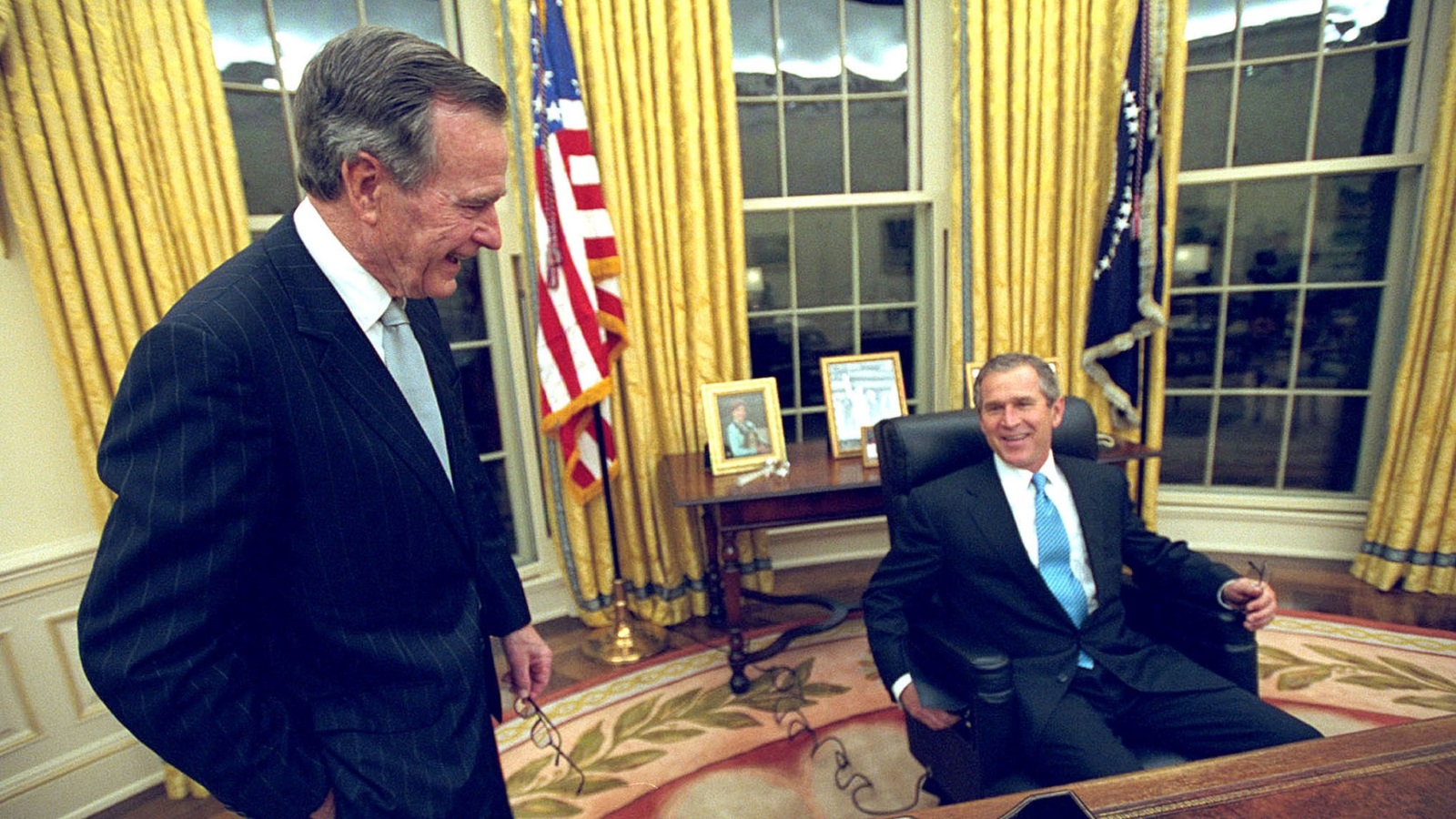 الرئيس جورج بوش الابن جالسا بالمكتب البيضاوي في 20 يناير/كانون الثاني 2001 بينما يشاركه اللقطة والده الرئيس جورج بوش الأب (غيتي)